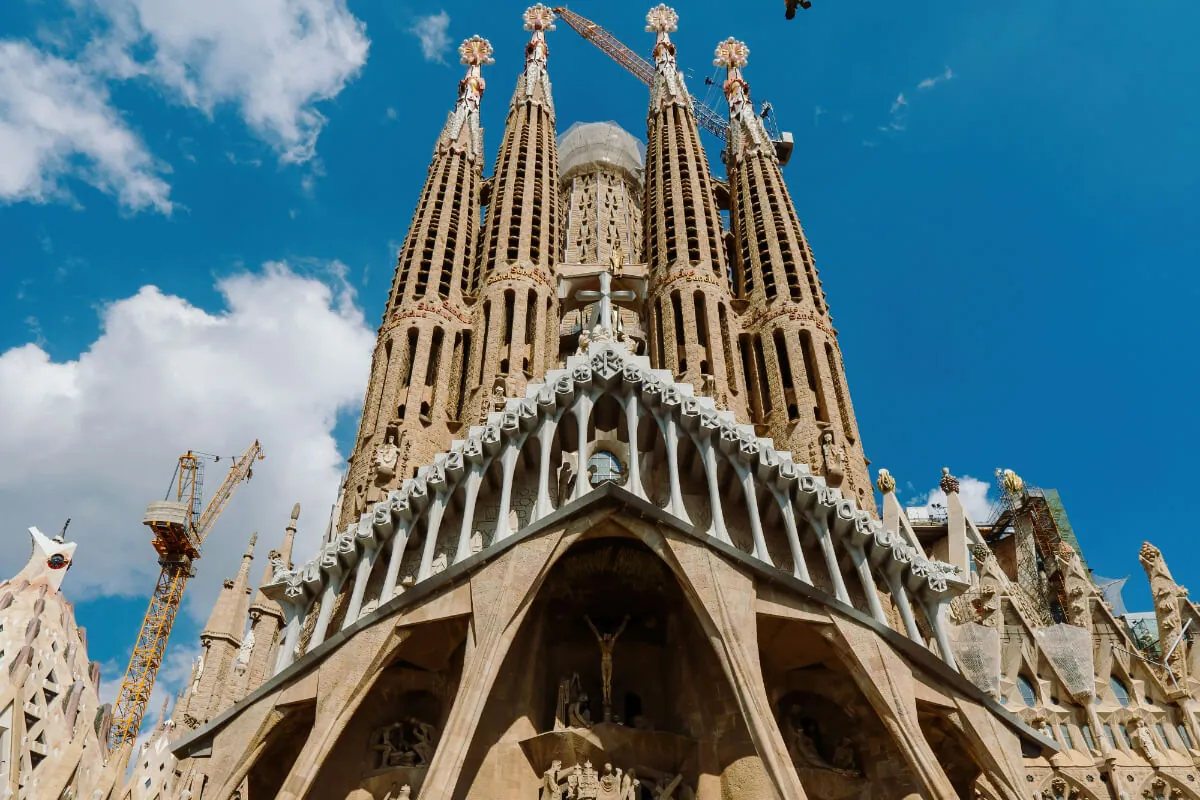 Barcelona ikonikus Sagrada Família temploma, barna tornyaival és kék éggel a háttérben. Építkezési daru a bal oldalon.