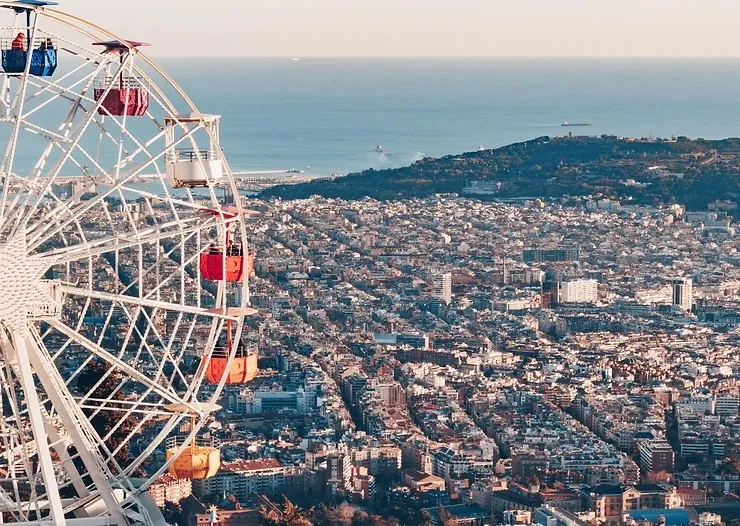 Tibidabo retro vidámpark. Óriáskerék színes kabinokkal balra, háttérben városkép és tengerpanoráma. Nyugodt, derűs hangulat.