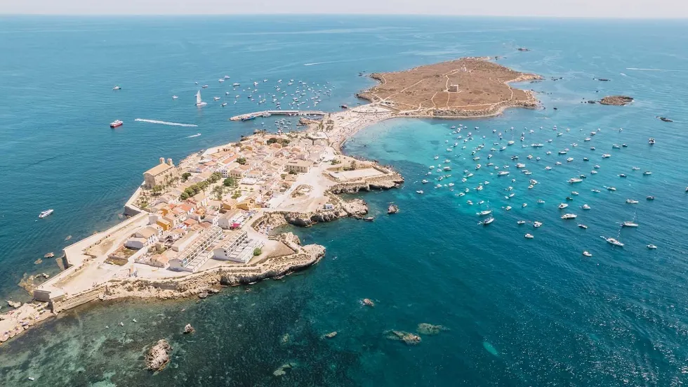 Légi felvétel Tabarca sziget (alicante) óvárossal, körülötte sok hajó a kék tengeren. Világos épületek és sziklás partvonal látható. Nyugodt hangulat.